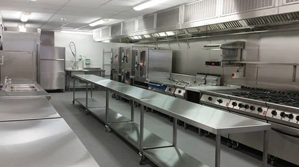 Clean stainless-steel commercial kitchen with prep tables and cooking line