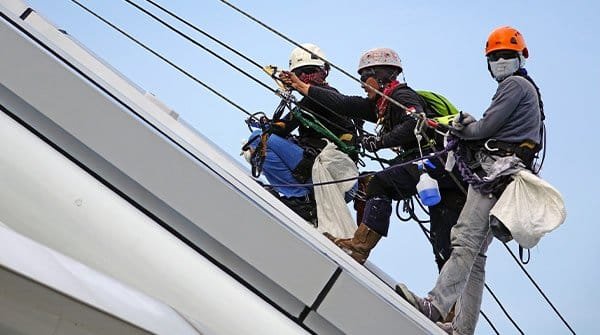 Workers in harnesses and helmets using fall protection on a sloped roof