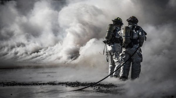 Emergency responders in protective gear moving through heavy smoke