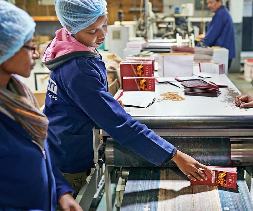 Production line workers in hairnets inspecting packaged goods on a conveyor