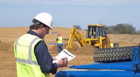 Safety consultant in a hard hat and hi-vis vest reviewing a checklist on a construction site