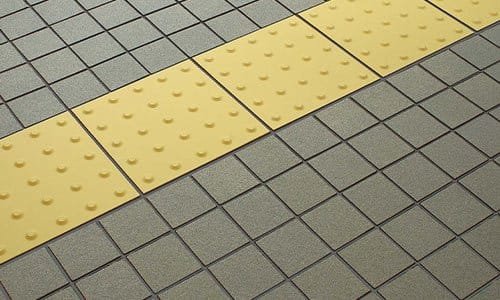 Yellow tactile safety tread tiles set into grey paving